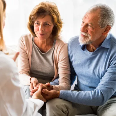 A senior couple, sitting down and holding hands, consulting a doctor at an appointment.