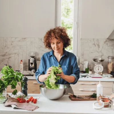 A woman making a bowl of salad in the kitchen. 
