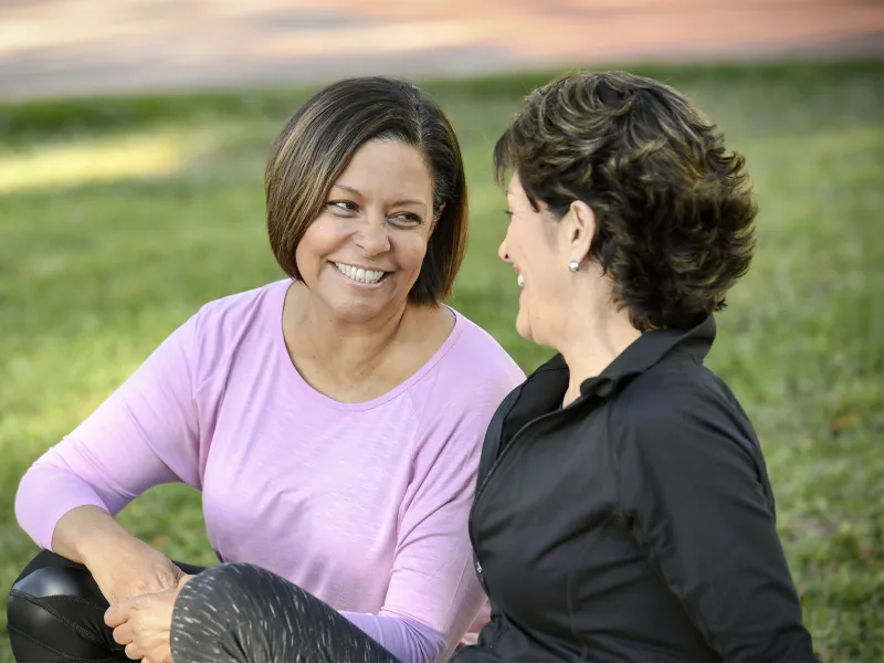 Two smiling women sitting outdoors talking