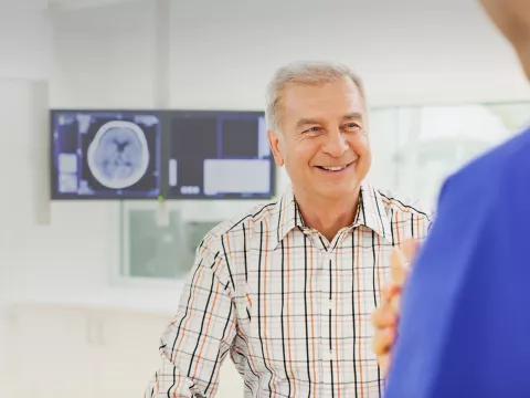 Man speaking with a doctor with imaging results on a screen behind him