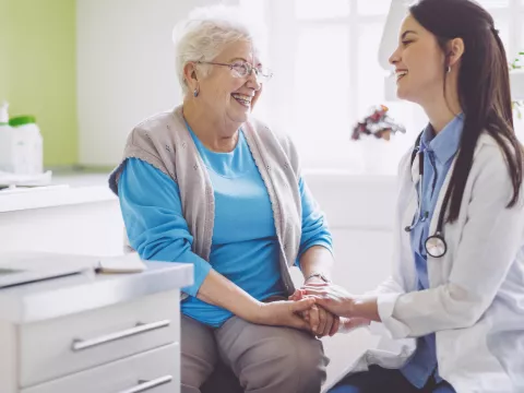 An older woman laughs with her doctor during a visit.