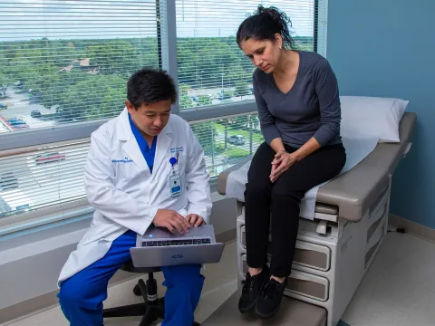 Iswanto Sucandy showing patient a something on a laptop while she's sitting on examination table.