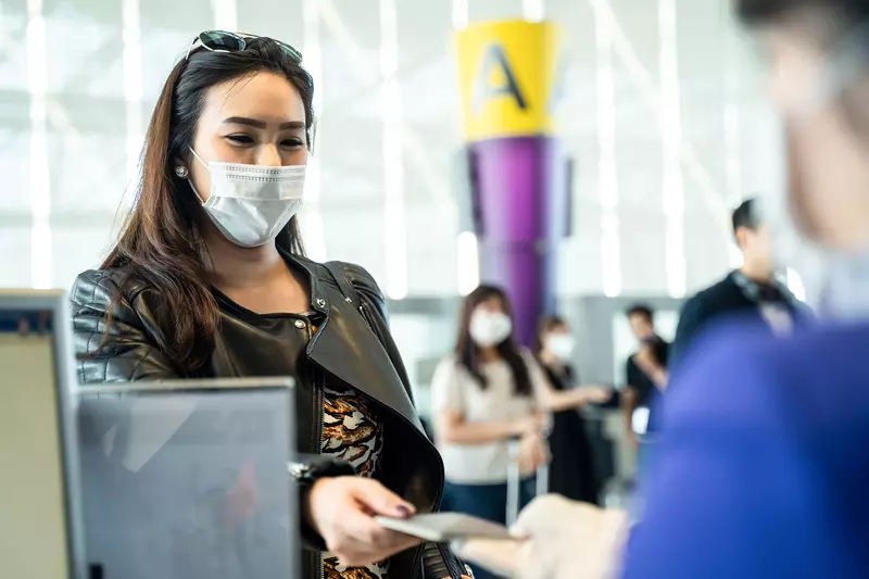 Lady checking in for a flight at an airline counter wearing a covid mask