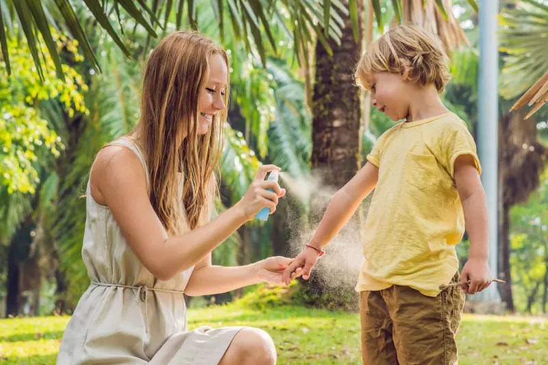 A Mother Sprays Her Young Son with Bug Spray in a Park
