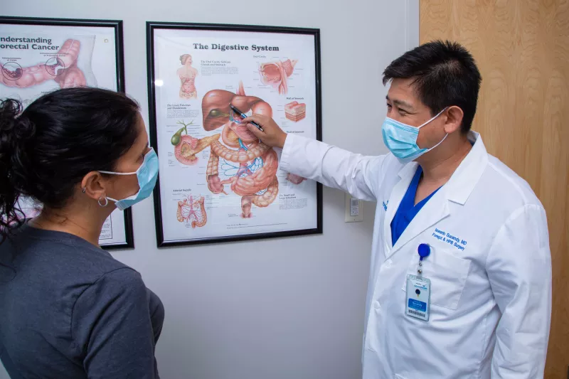 Dr. Sucandy speaking to a patient and pointing at a digestive system diagram.