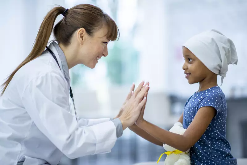 Encouraging doctor with young cancer patient, they are clapping hands together.