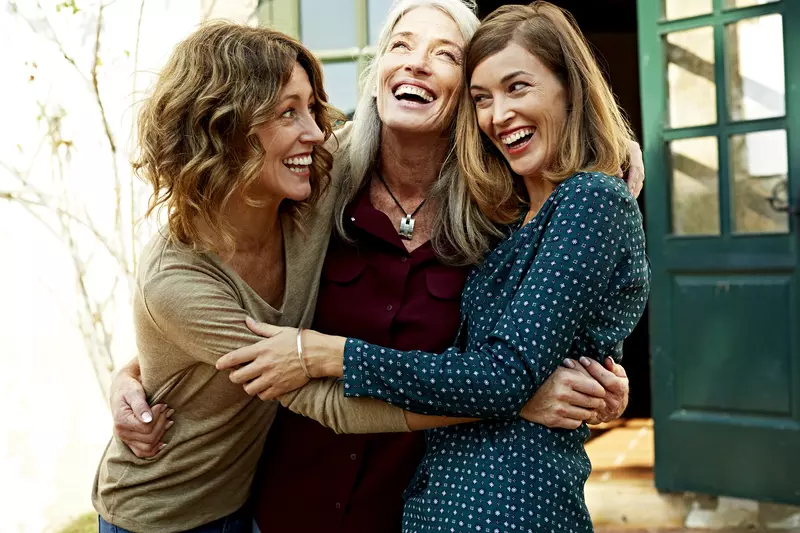 Three women celebrate their health by hugging each other.