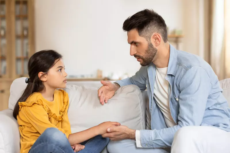 A father talks with his daughter while both are sitting on a couch.