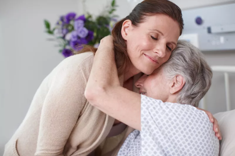 An adult daughter hugs her mom in the hospital.