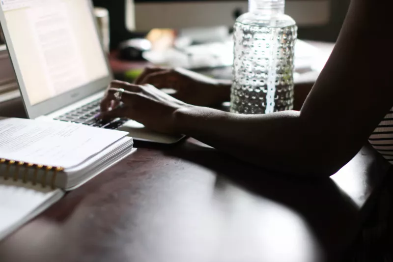 Woman typing on computer with water bottle