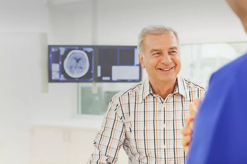 Man speaking with a doctor with imaging results on a screen behind him