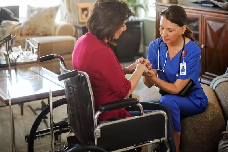 Woman in a wheelchair praying with a home care nurse.