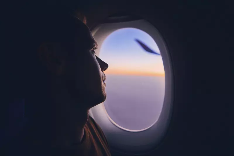 A man looks out the window of a plane during sunset.