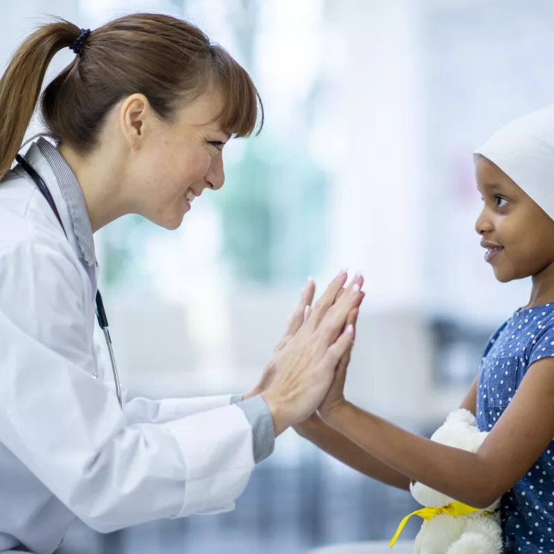 Encouraging doctor with young cancer patient, they are clapping hands together.