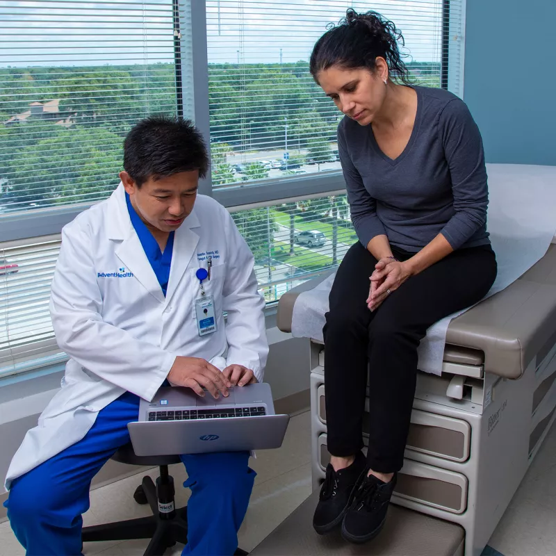 Iswanto Sucandy showing patient a something on a laptop while she's sitting on examination table.