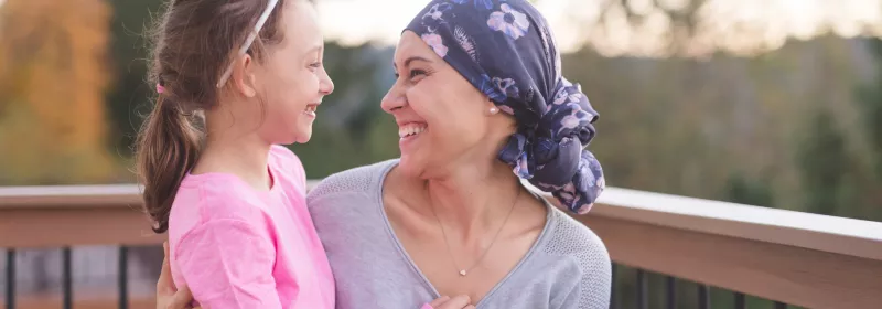 A mother and cancer survivor is sitting, with one arm around her daughter.