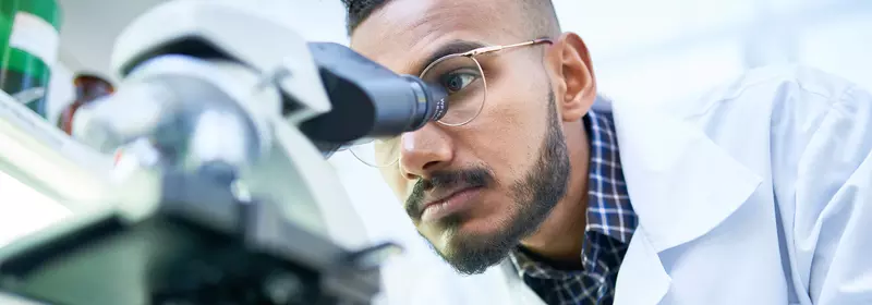 Man looking into a microscope to analyze the results of a clinical trial.