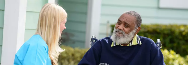 Elderly man in a wheelchair outside speaking to a nurse.